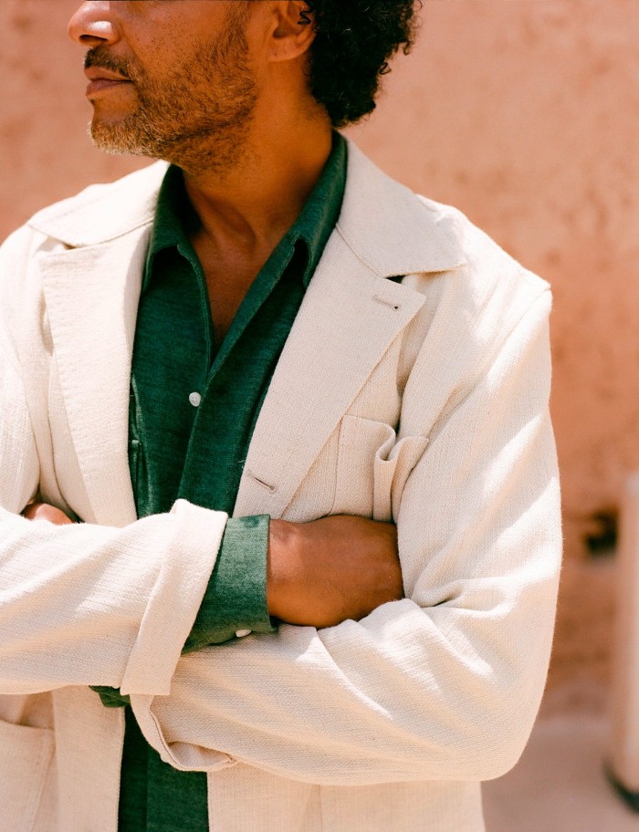 A look from The Anthology’s spring/summer 2024 campaign: a man wearing a white jacket and a green shirt standing with his arms folded, with his face in profile