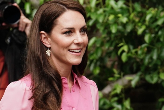 Catherine, Princess of Wales is smiling warmly. She is wearing a bright pink, long-sleeved dress with gold drop earings.