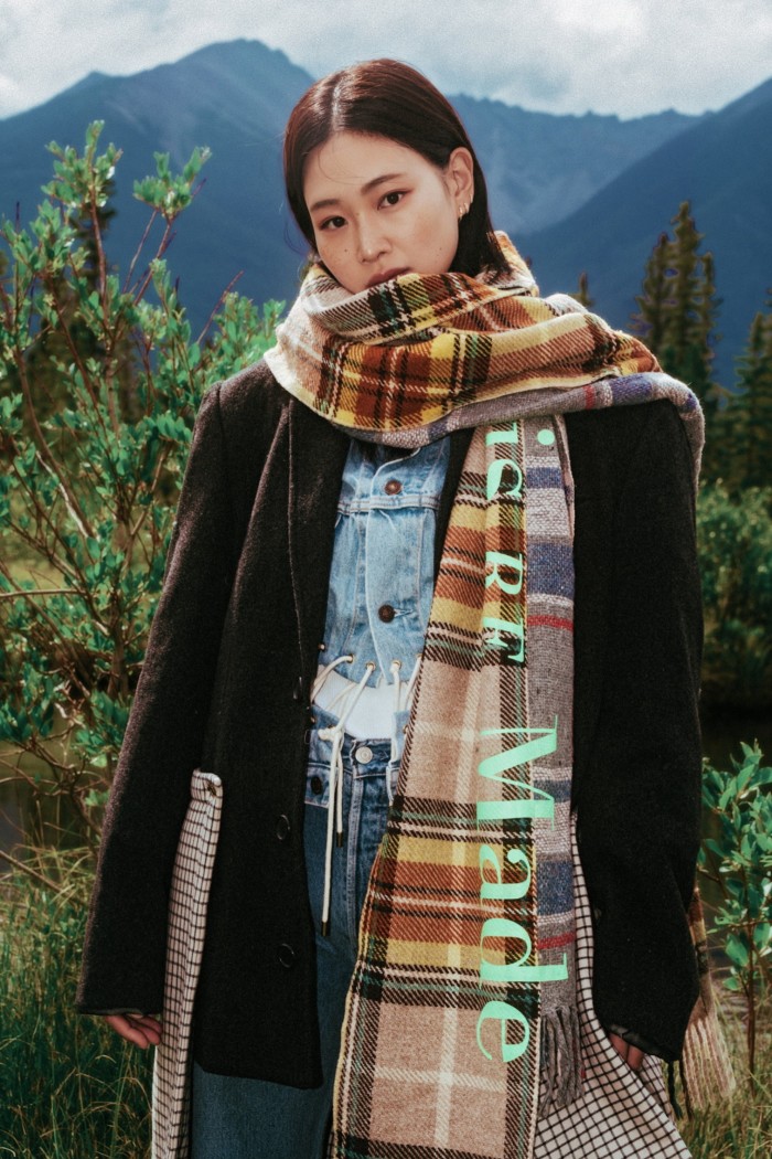 A woman in the countryside wears a plaid scarf and dark blazer