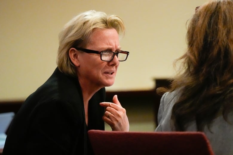 A woman leans over while gesturing with her hands. 