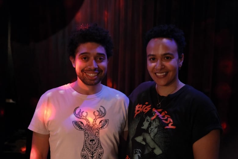 A person with curly hair and a white shirt smiles next to a person with short hair and a black shirt.