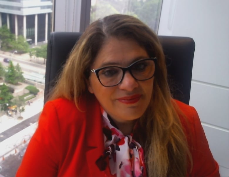 Woman with glasses and a red blazer sitting in office with city view