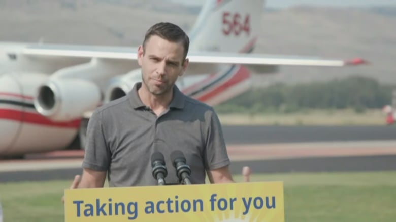 A man stands behind a podium with an airplane in the background.