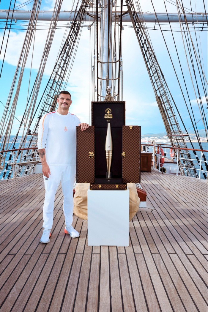 An athlete opens a designer trunk to reveal an Olympic torch inside 