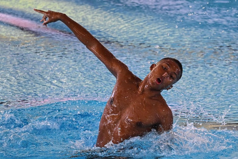 A man doing artistic swimming moves in a swimming pool has his right arm pointed at the upper-left corner and his head titled to the bottom-right side of the picture.