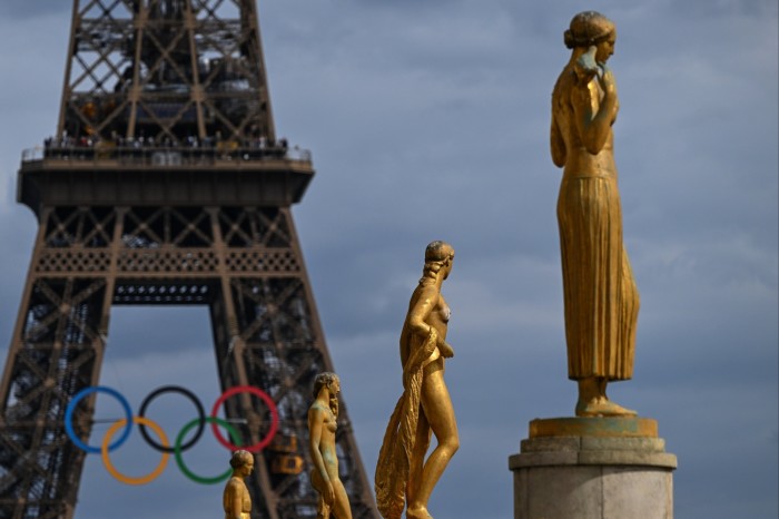 the rings span the bottom of the tower; bronze female statues are also visible against the sky