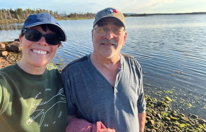 A smiling woman and man pose for a selfie by a rocky shore. 