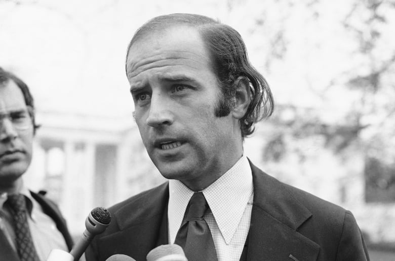 A black and white photo of a young, thin, slightly balding man.