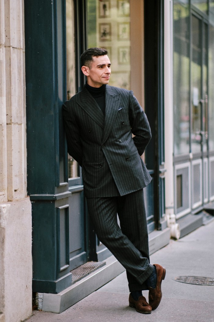 A model in black pinstripe double-breasted suit leans against a building