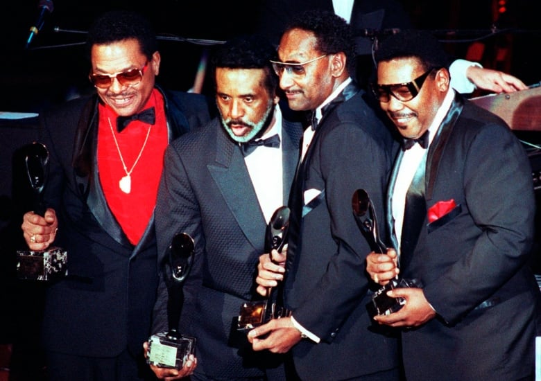 Four men wearing dark suits and holding up awards pose for a photo.