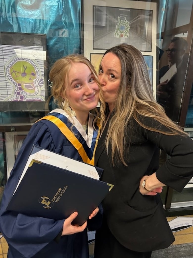 A woman opens her eyes wide as she kisses the cheek of a younger woman in a blue and yellow robe. 