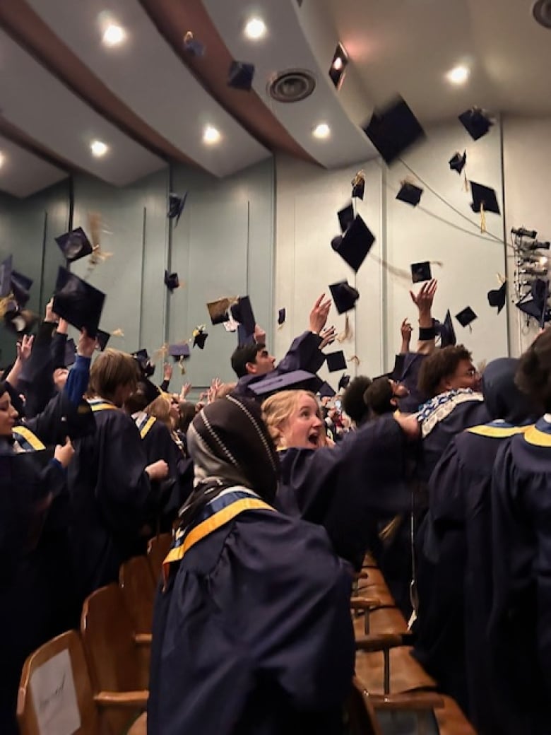 Young men and women in navy blue robes throw square caps with tassels in the air.