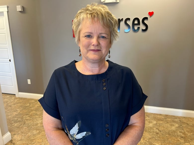 A woman with short blonde hair and a dark blue shirt stands in front of a sign reading PEI Nurses' Union