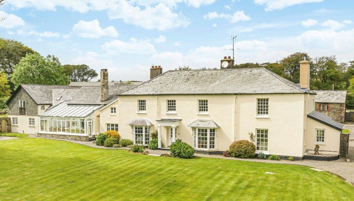 A large cream-coloured house with a glass conservatory and large, neat lawn