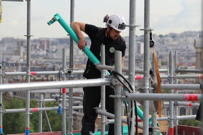 A man wearing a white hard hat and black clothes repairs a building.