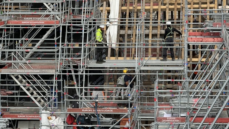 A far view of multiple floors of scaffolding, with workers repairing the building.