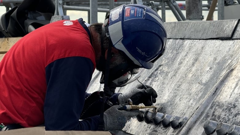 A man in a red shirt with dark blue sleeves repairs a building.