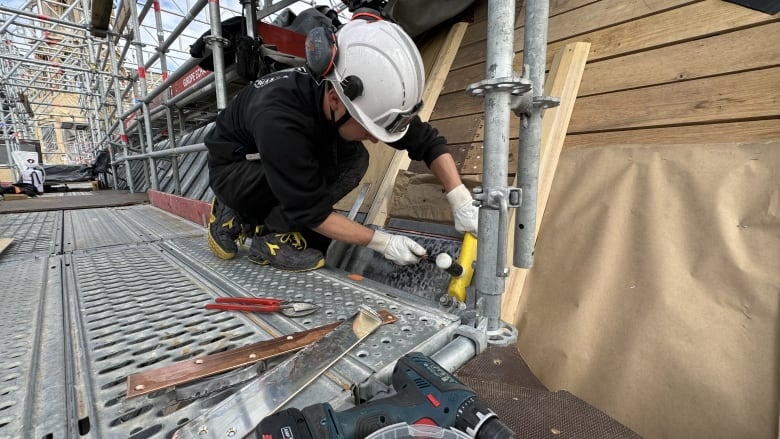 A man in a white hard hat fixes a building.