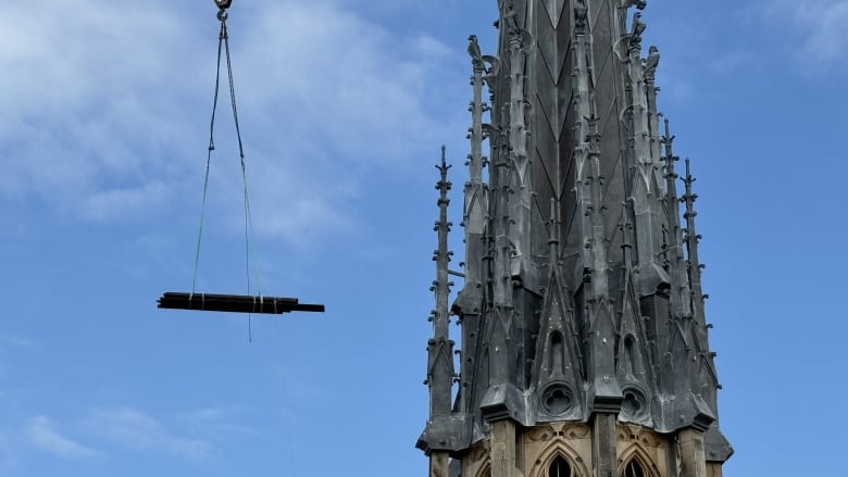 A view of a cathedral spire. On the left, planks hang. 