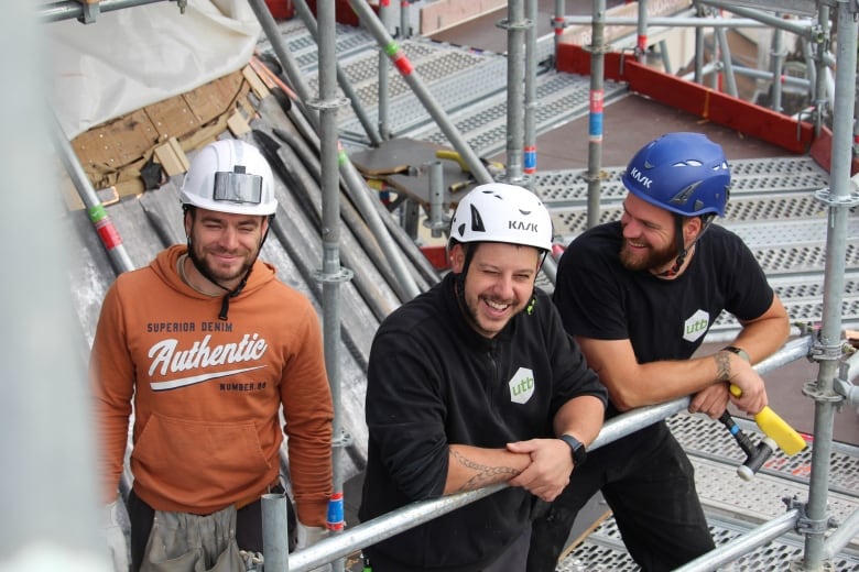 Three men in hard hats stand and laugh.