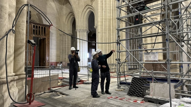 Three people stand inside a cathedral under construction.