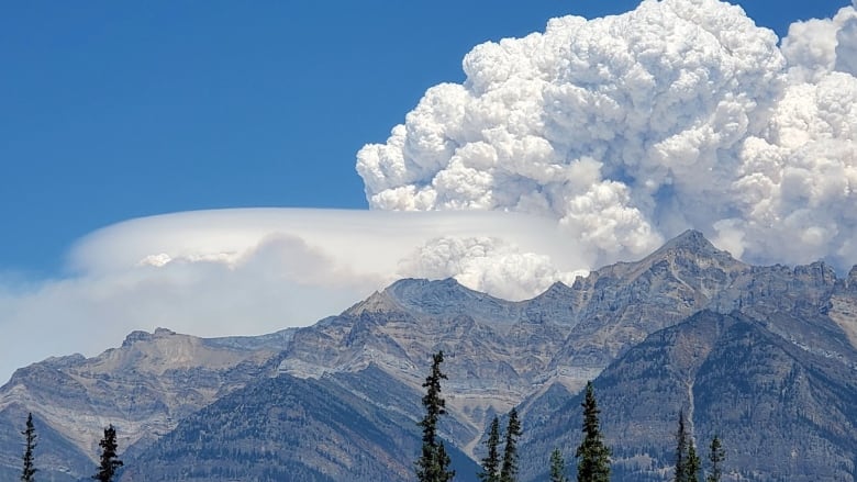 White smoke billowing into bright blue skies with mountains in the foreground.