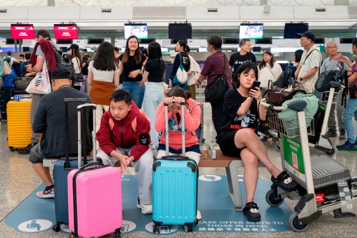 Passengers wait in line and sit on a bench at the Emirates airline check-in desk