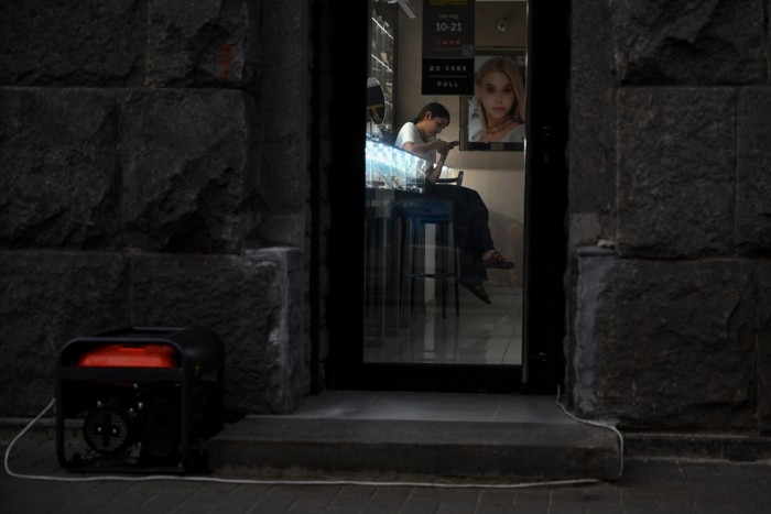 An employee of a jewlery shop looks at her smartphone, while a power generator works outside