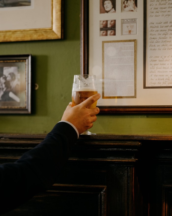 A man’s hand holding a pint of beer on a wooden shelf in Sandy Bell’s 