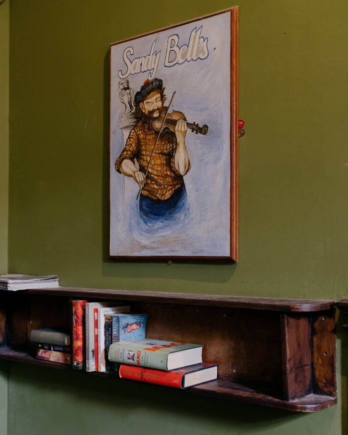 An illustrated poster of a man wearing a tam o’shanter and playing a fiddle beneath the words ‘Sandy Bell’s’ on a wall of the pub