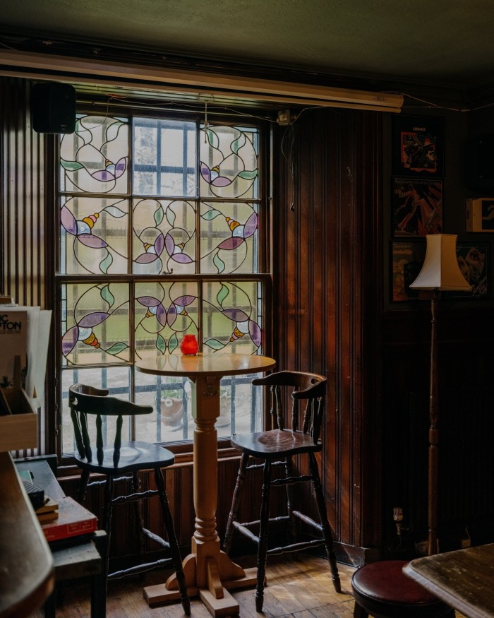 A tall wooden table for two in front of a stained-glass window in the St Vincent Bar 