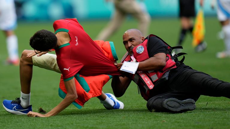 A steward catches a pitch invader during the men's Group B soccer match between Argentina and Morocco at Geoffroy-Guichard Stadium at the 2024 Summer Olympics, Wednesday, July 24, 2024, in Saint-Etienne, France. (AP Photo/Silvia Izquierdo)