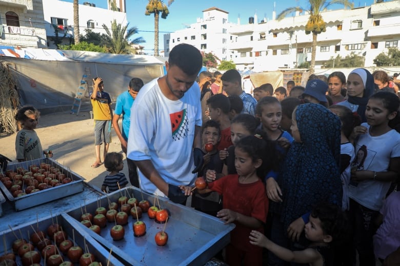 A man passes out candied apples to kids outside