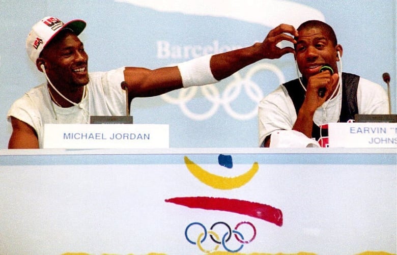 Two basketball players speak at a podium.