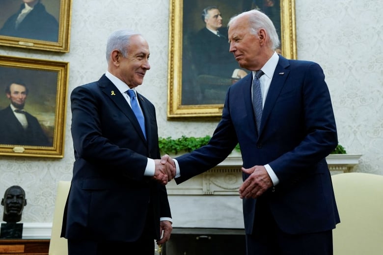 Two men in suits shake hands in an ornate office.