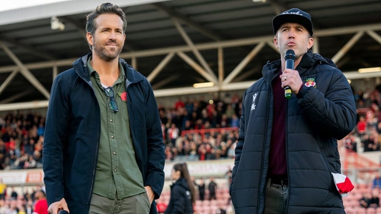 Two male actors address fans at a soccer stadium.