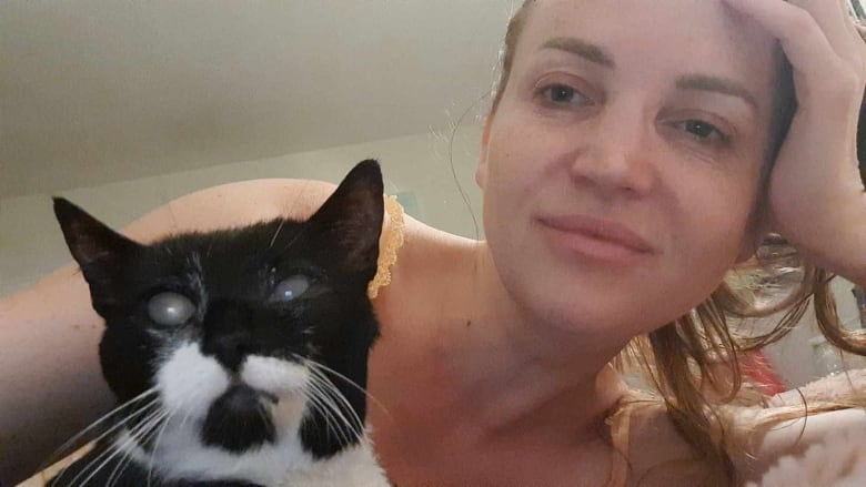 A woman sits on a bed with a cat.