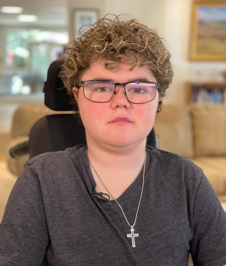 A young man with curly hair and a cross on a necklace.