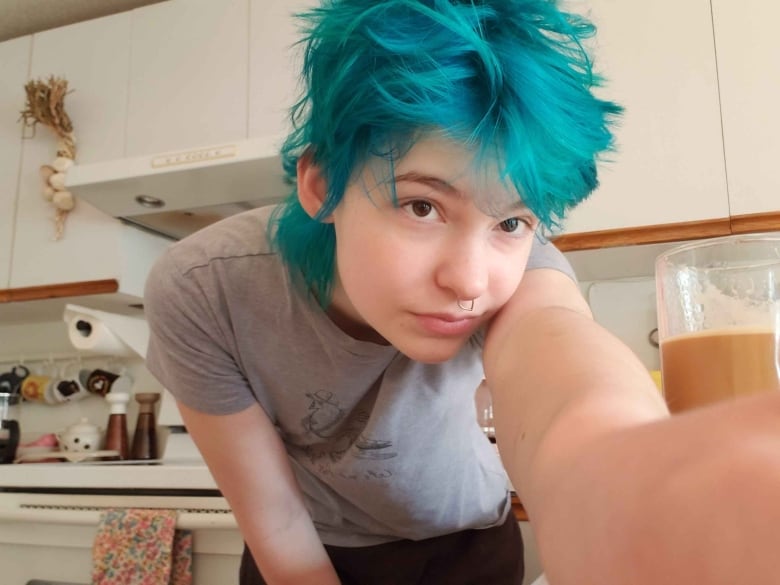 A person with blue hair poses for a selfie in a kitchen.  