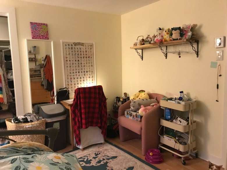 A bedroom with a pink armchair, stuffed toys on bookshelves and clothing in a hamper. 