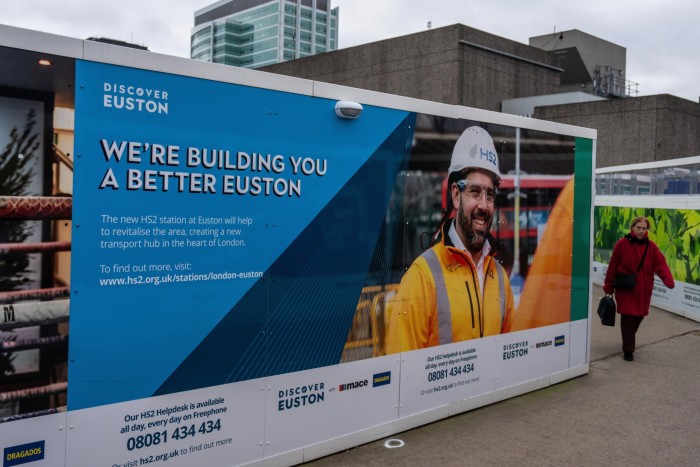 A woman walks alongside hoarding surrounding the HS2 site in Euston in London