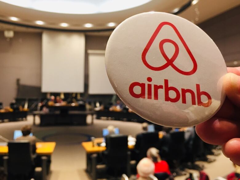 An Airbnb pin is held up against the backdrop of Ottawa City Council. 