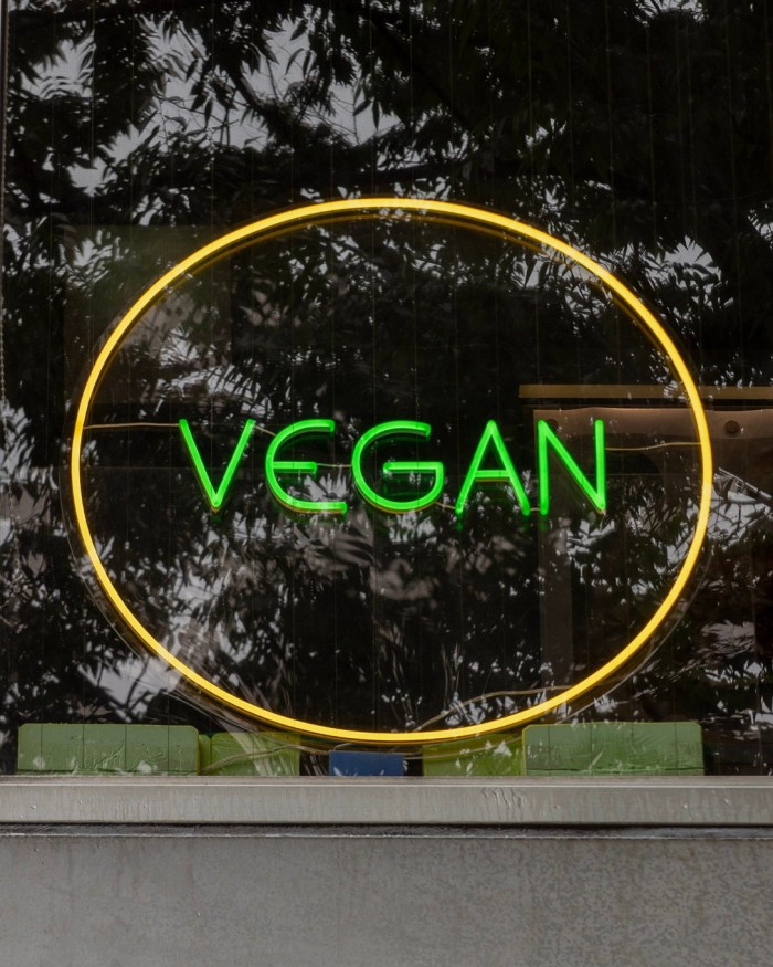 A green neon sign that says ‘Vegan’ surrounded by a yellow circle in the window of Vegan Bistro Jangara