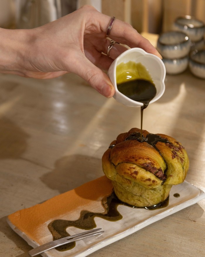 A hand pouring a brown liquid over Café Chairo’s matcha cinnamon roll