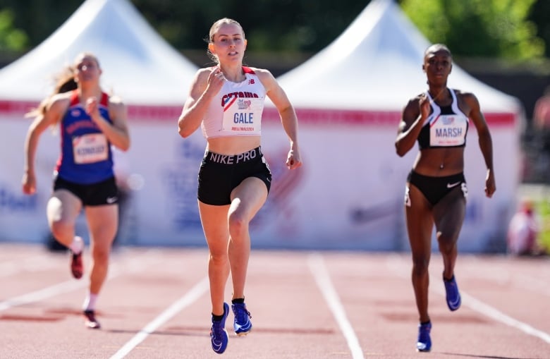 A woman runs on a track, with several other runners visible in the background.