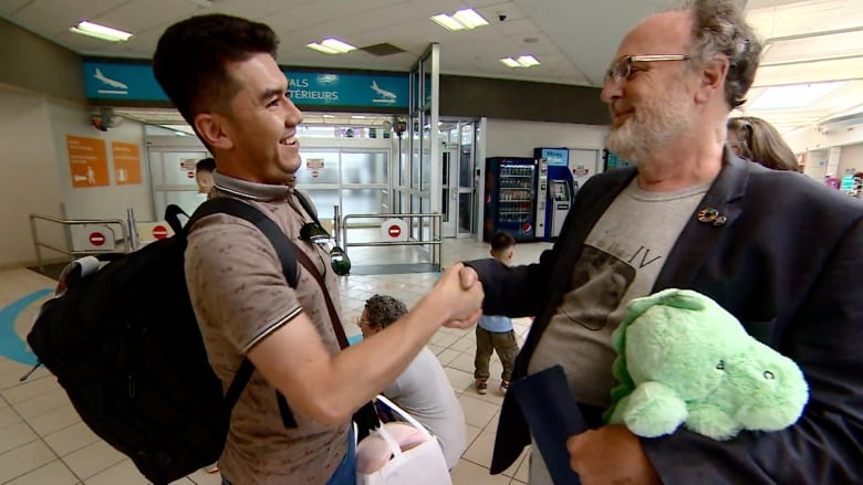 Two men shake hands at an airport.