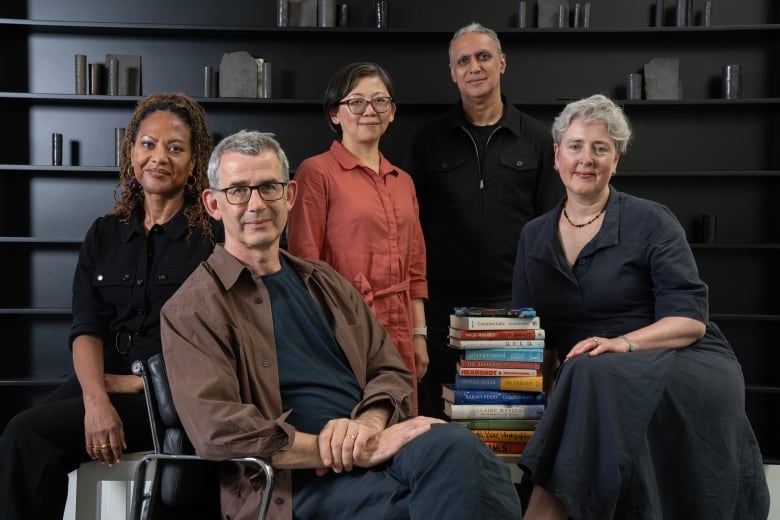 A black woman, a white man, an Asian woman, a brown man and a white woman pose with a stack of 13 books. 