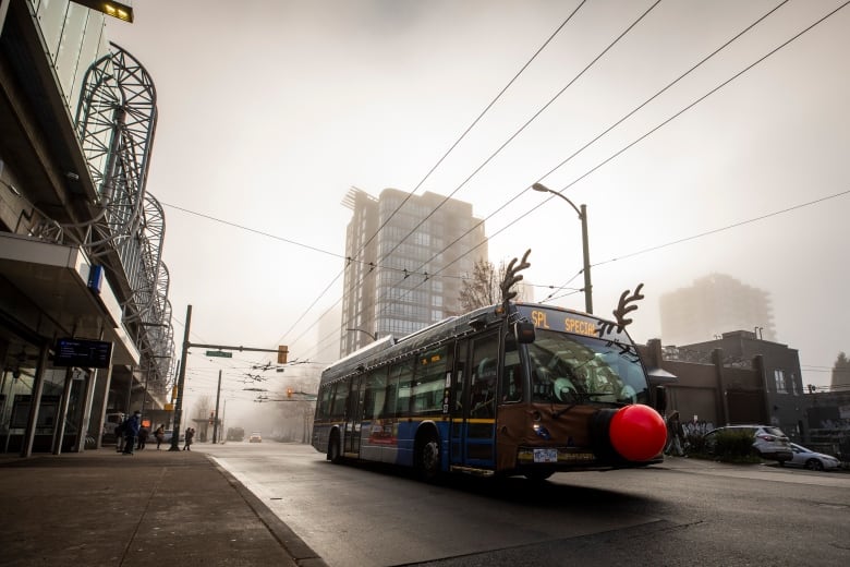 A bus with a big red nose on the front of it, and reindeer antlers, is pictured amid foggy conditions on a city road.