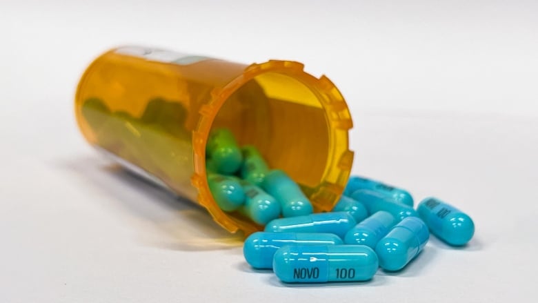 Several blue capsules spilling out off an orange prescription bottle onto a white surface. 