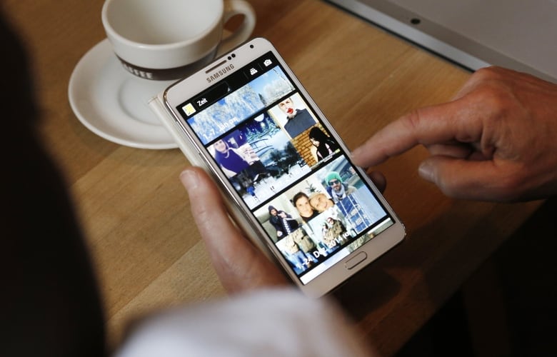 A close-up image of a senior holding a smartphone and scrolling through thumbnails of online videos.